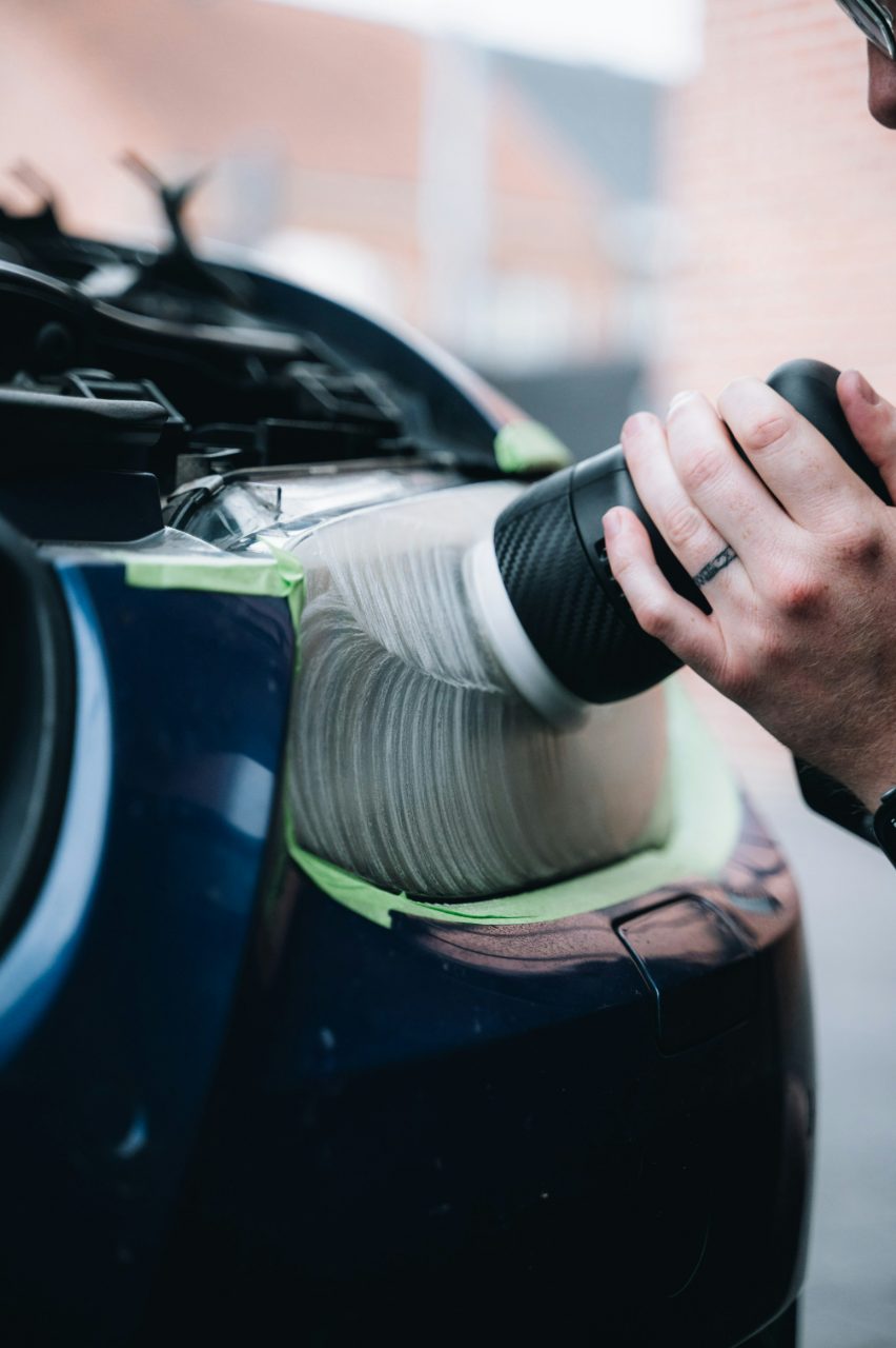 A technician machine-polishing a taped-off headlight