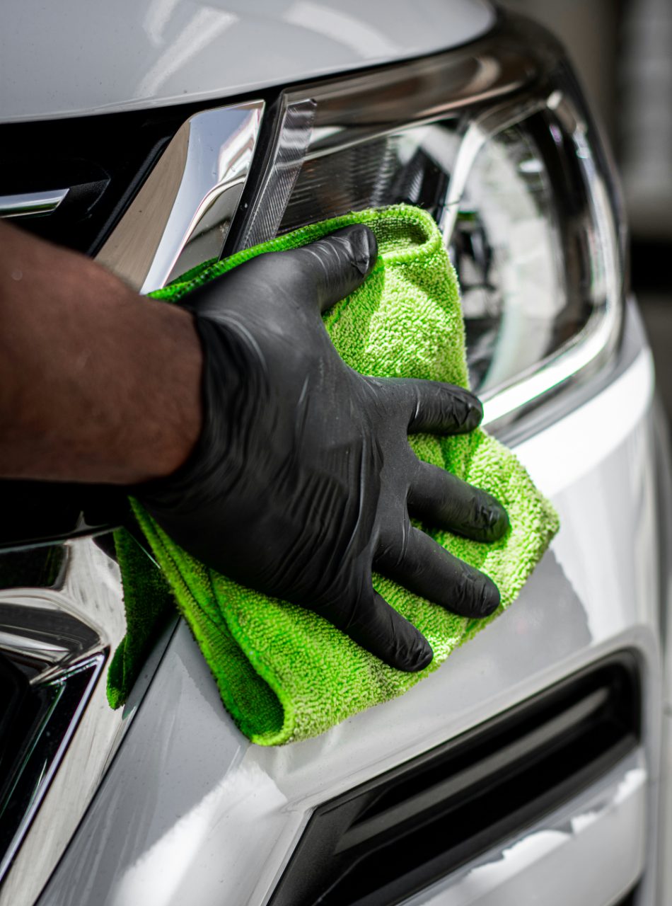 Technician wiping a polished headlight with a green microfiber cloth